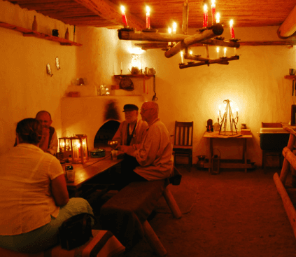 The candlelit cantina: a chandelier of candles over people talking at plank tables inside adobe walls