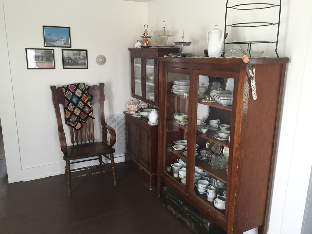 Oak china cabinets full of dishes beside a pressed-back chair with a granny-square afghan