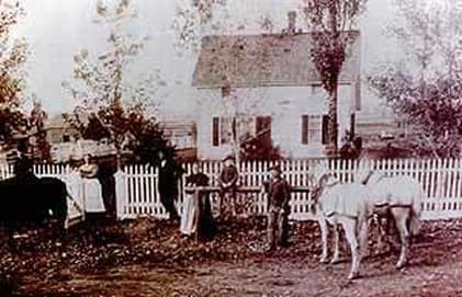 The Donelson family in period dress posed in front of the house and picket fence with white horses, 1893