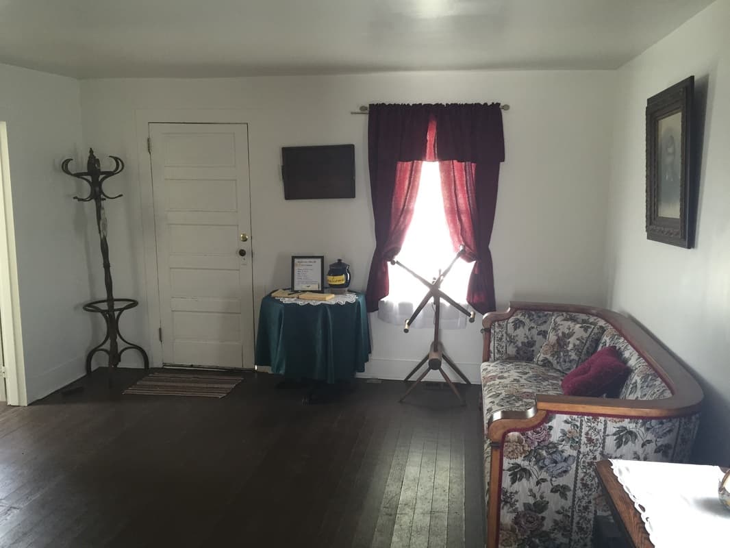 The parlor with a floral settee, a bentwood hat stand, a yarn swift and red curtains