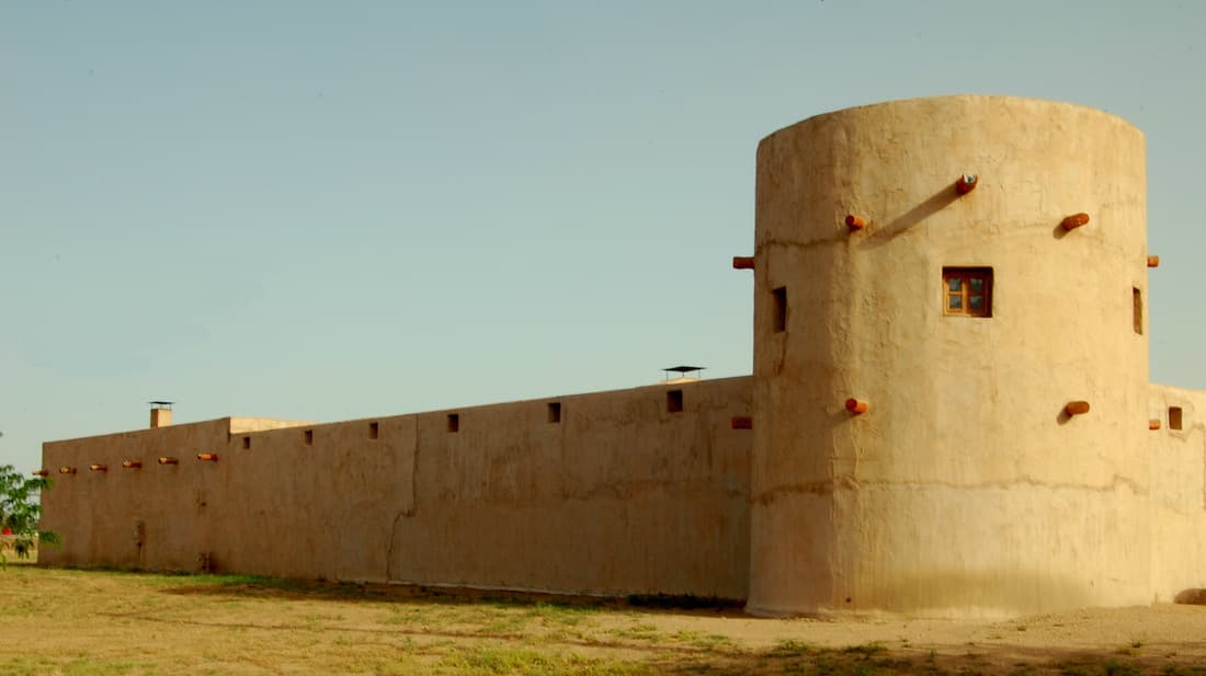 The round adobe bastion of Fort Lancaster beside the fort's long wall, with cedar beam ends jutting from the plaster in golden evening light