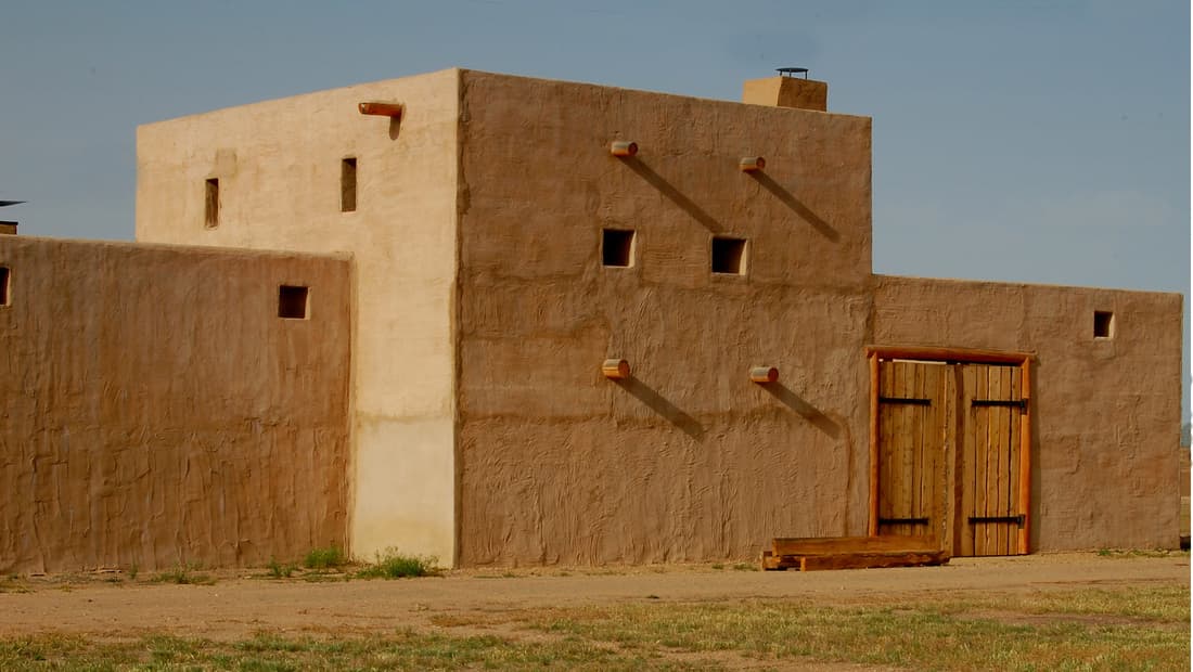 The fort's two-story adobe trade block with projecting log vigas above the main timber gate