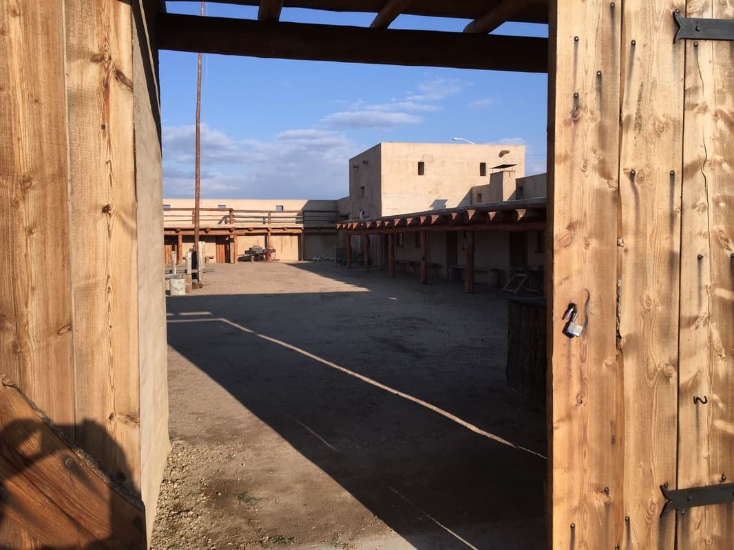 Looking through the open timber gate into the fort courtyard, with the covered portal, the flagpole and a wagon