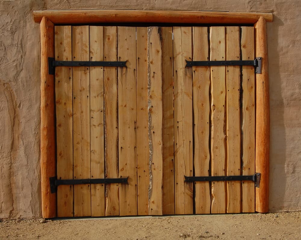 Rough-sawn plank double doors with forged iron strap hinges, set in a log frame in the adobe wall