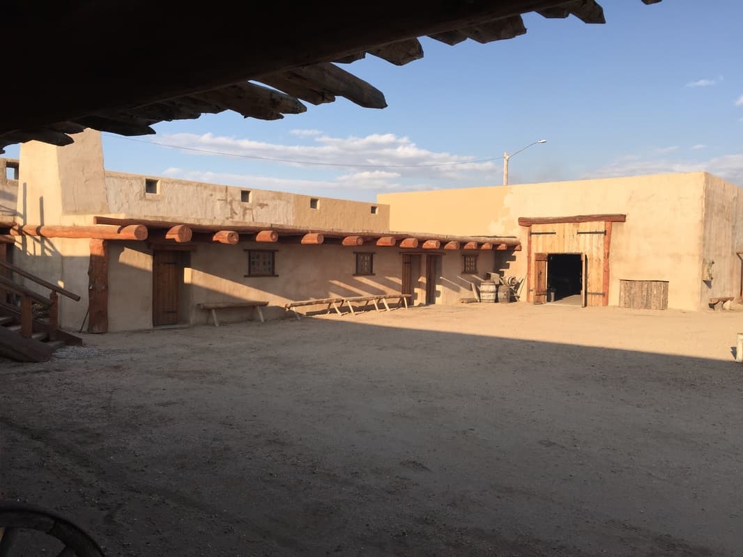 The courtyard seen from under the portal roof: rooms with plank doors, barrels and the open gate