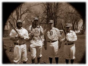 Four vintage baseball players in old-time uniforms holding bats