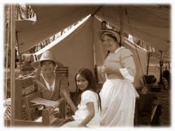 A woman in period dress with two girls inside a canvas tent