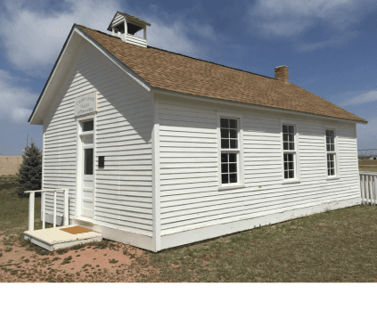 The white one-room Independence School with its bell cupola and brick chimney under a blue sky