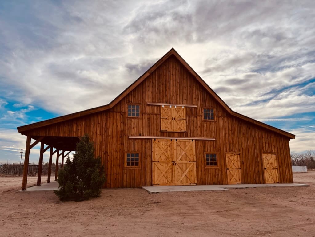 The finished post and beam barn: a cedar board-and-batten gable with cross-buck sliding doors and an open lean-to wing