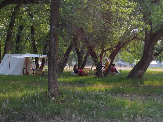 People in period dress seated in a circle under the cottonwoods in low sun
