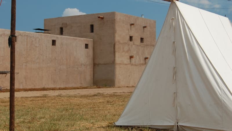 A white wall tent in front of the fort's adobe tower and wall