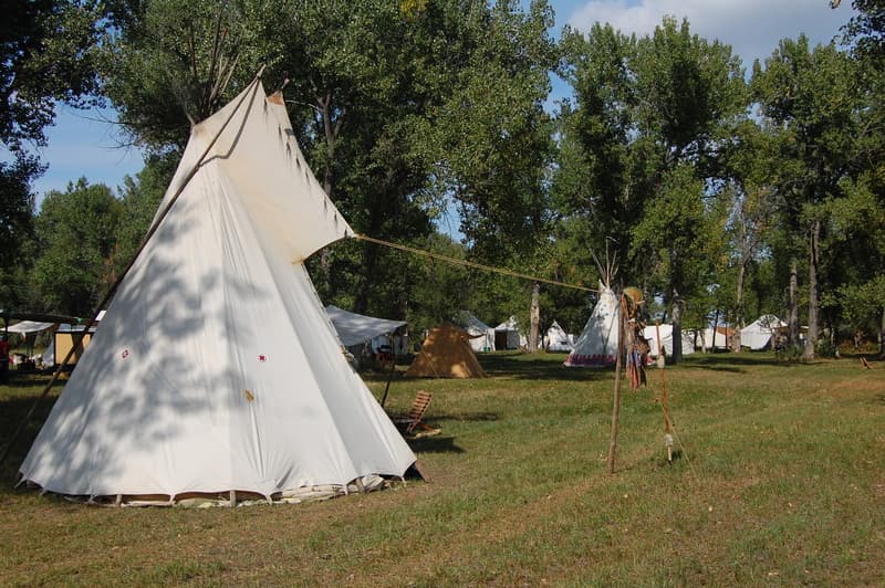 A big white tipi under the cottonwoods with more lodges behind
