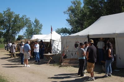 Visitors browsing a trader's wall tent hung with goods