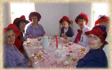 Ladies in red hats at a tea table in the Donelson House