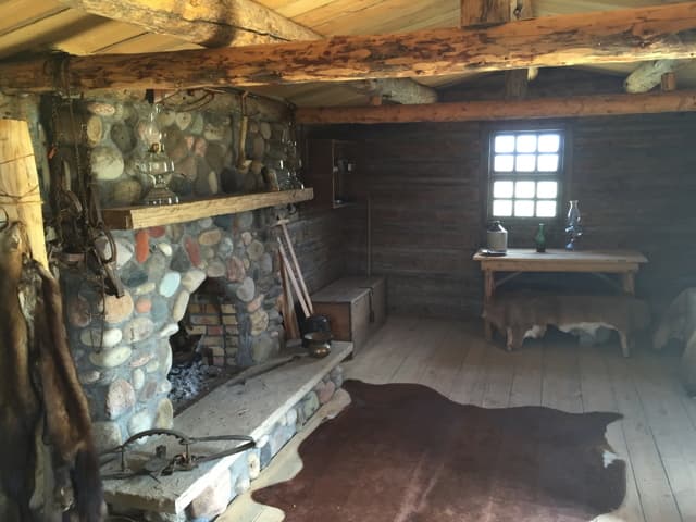 Inside the cabin: a river-rock fireplace with an oil lamp on the mantel, a bison hide rug, traps and furs