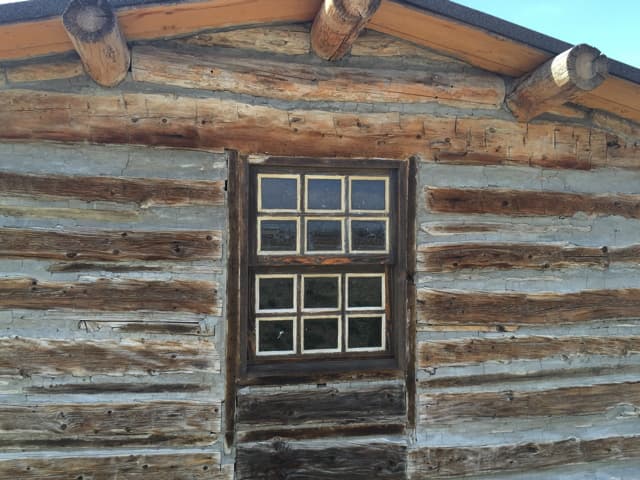 The cabin's small window set in weathered logs with white chinking
